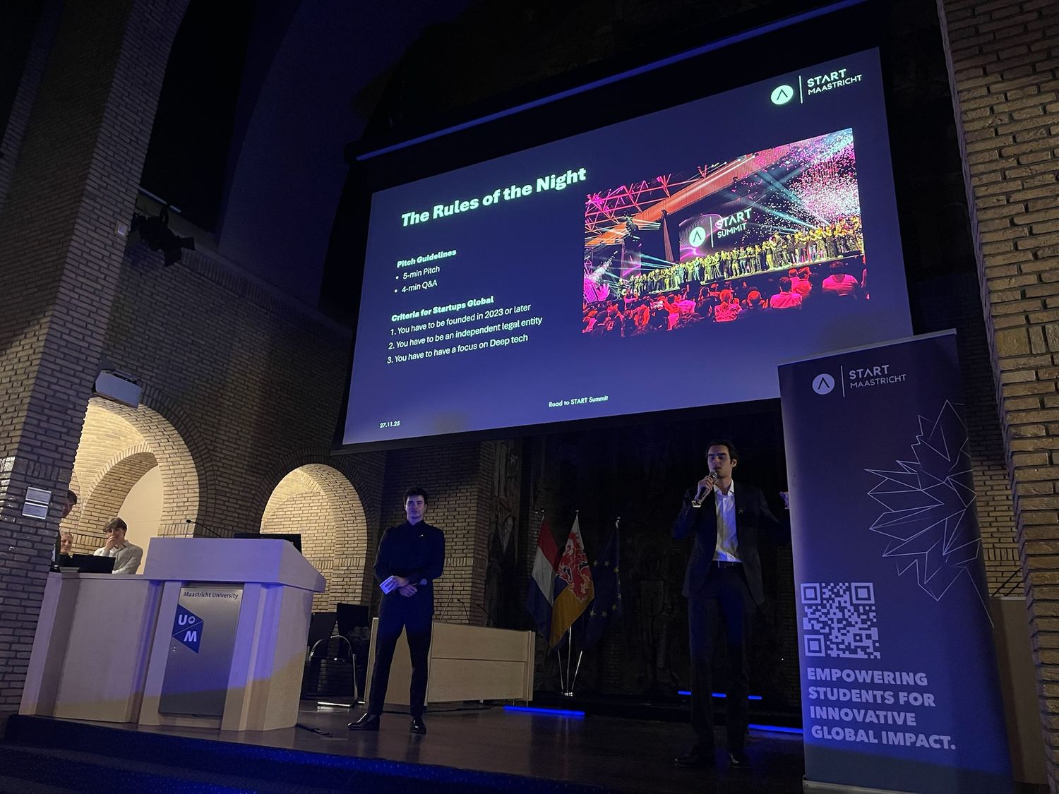 Two hosts on stage at Road to START Summit in a Maastricht University hall